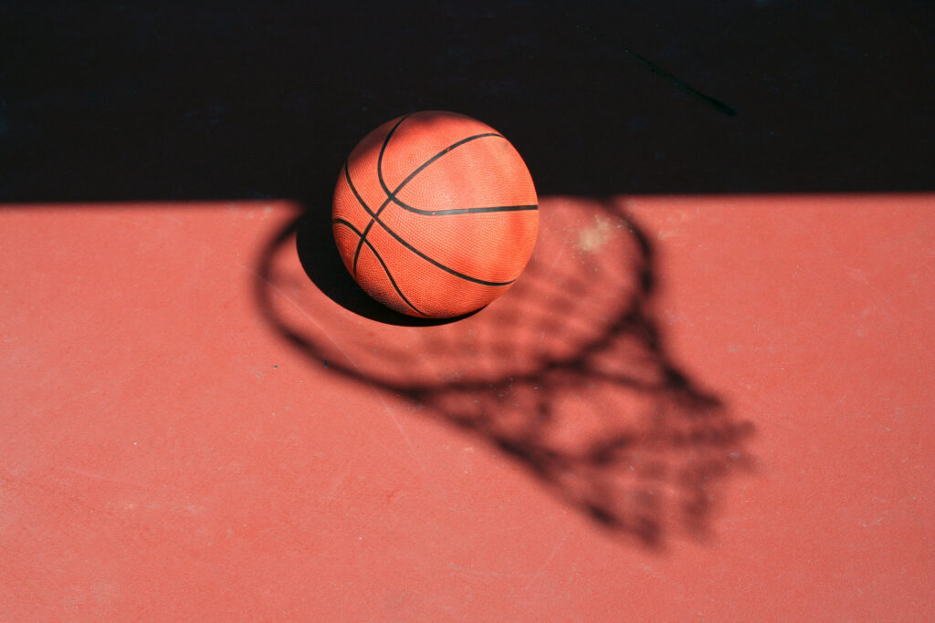 A Basketball and net shadow on a red court